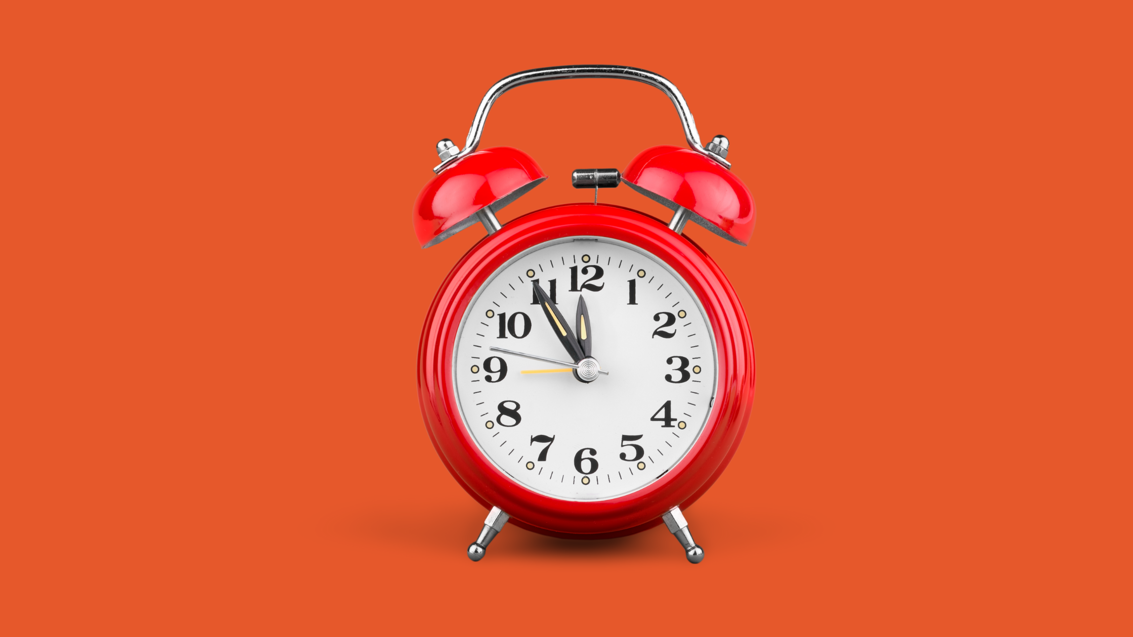 a old fashioned red enamel alarm clock on an orange background