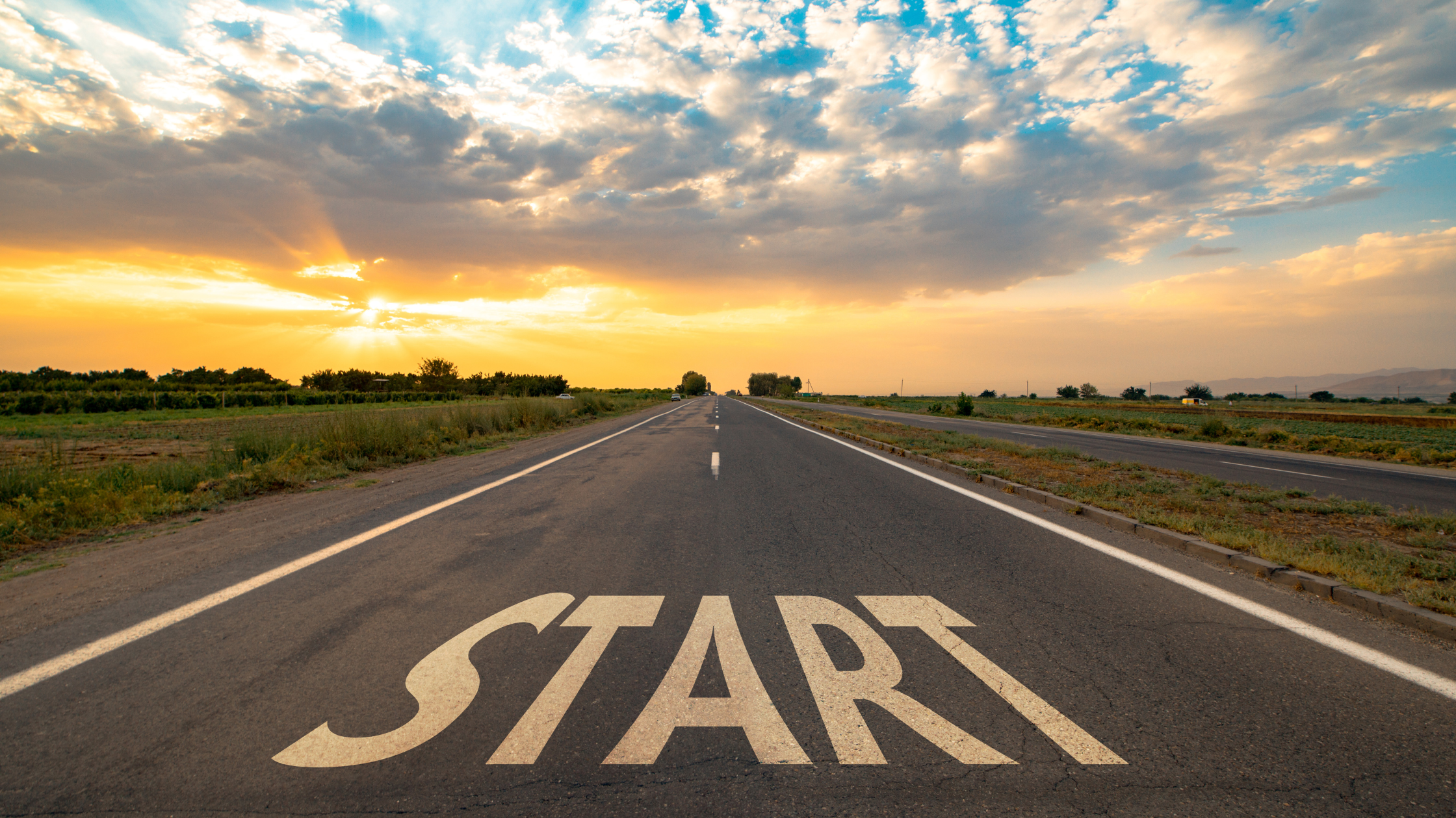 a photograph of a road in the countryside, leading to the horizon with the sun rising. On the road, in the foreground, is the word 'START'